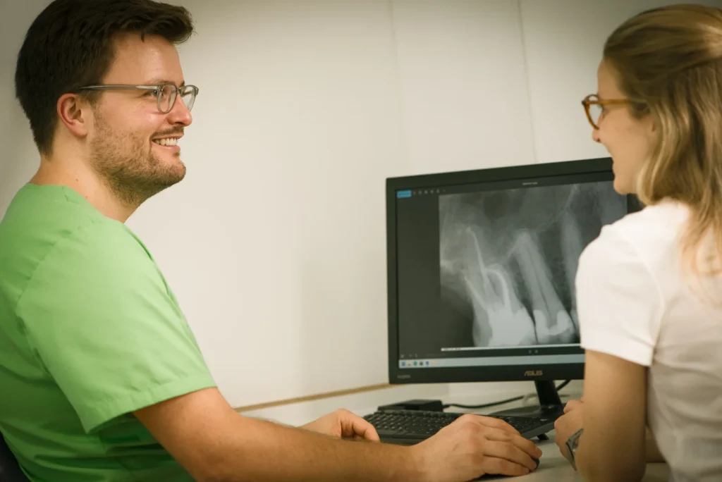 Dr. Morlock im Gespräch mit Patientin an Computer mit Röntenbild Zahnwurzel